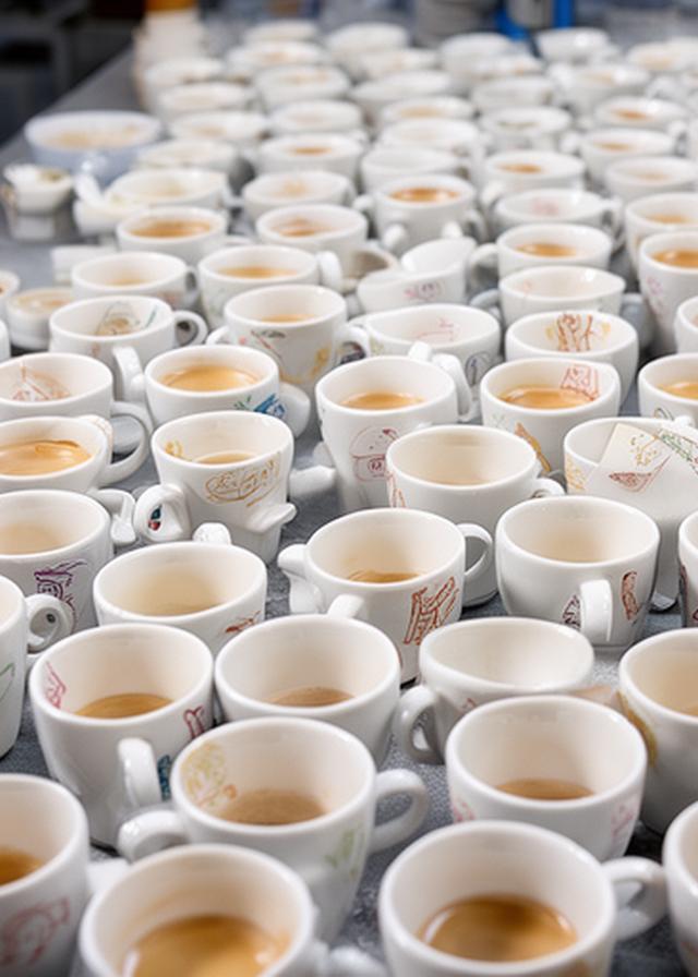 Reihe bedruckter Espressotassen mit eingebranntem Firmenlogo auf einem Produktionstisch in einer hellen Werkstatt